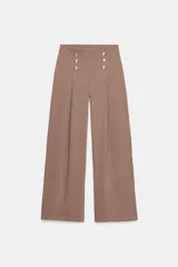 Pantalón de tiro alto con pierna ancha, confeccionado en sarga color tostado. Presenta detalle de doble hilera de botones metálicos dorados en el frente y pinzas verticales.
