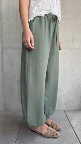 Pantalón tipo babucha de color verde militar, con cintura elástica fruncida y cordón ajustable. Cuenta con diseño amplio y puños elásticos en los tobillos.