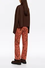 Pantalón de denim de corte recto y tiro alto, con diseño de cinco bolsillos y cierre frontal con botón y cremallera. Presenta un estampado de manchas oscuras sobre base de color terracota.