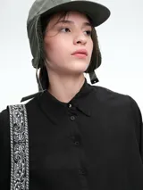 Camisa de corte oversize color bordó, con cuello clásico, cierre frontal de botones y mangas largas amplias con puños anchos. Presenta un diseño de caída fluida con bajo redondeado y levemente más largo en la parte posterior.