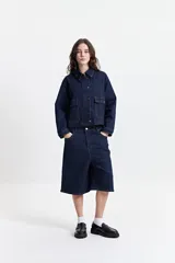 Campera de jean de mezclilla oscura, corte relajado, con cuello y bolsillos de parche con tapa y botón en el pecho. Presenta costuras en tono naranja/marrón claro.