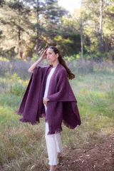 Ruana de lana merino extrafina con tejido texturizado, diseño envolvente y flecos en los extremos. Prenda versátil de corte amplio y sin género.