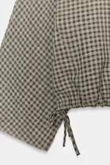 Camisa tipo capa de corte amplio y holgado, con estampado de cuadros vichy. Presenta cuello redondo, escote en pico en la espalda, mangas largas anchas y bajo ajustable mediante lazada lateral.