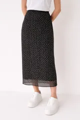 Falda midi de corte recto con estampado de lunares pequeños en color blanco sobre fondo negro. Presenta un detalle de transparencia en el ruedo.
