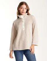 Buzo de tejido soft mohair con estampado zigzag en tonos beige y blanco. Presenta cuello polo, escote en V con botones a presión y manga larga amplia. El bajo tiene tajos laterales y apliques metálicos.