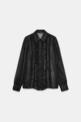Camisa de manga larga con cuello solapa, confeccionada en tejido semitransparente con hilo metalizado. Presenta volantes frontales decorados con abalorios y cierre frontal con botones ocultos.
