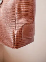 Bolso tote grande de cuero color marrón con textura tipo reptil. Tiene doble asa de hombro, cierre superior y bolsillo frontal con cierre. Incluye un dije colgante en forma de estrella con flecos plateados.