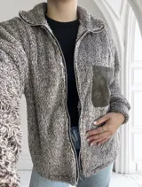 Campera de abrigo color marrón con textura de peluche, cierre frontal con cremallera y bolsillo de parche en el pecho.