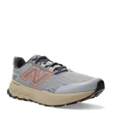 Championes de trail running New Balance modelo Garoe, color gris con detalles en naranja y suela en tono arena. Presentan tecnología Fresh Foam en la entresuela para mayor amortiguación y refuerzos en la puntera para mayor protección.