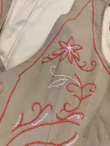 Chaleco reversible de acrocel de algodón color beige, liso de un lado y con bordado artesanal de flores y ramas en tonos rojos y amarillos del otro, con cierre frontal de botones de madera.