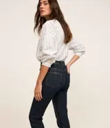 Pantalón de jean de corte slim, color azul oscuro, con trabillas en la cintura, cierre por botón y cremallera, bolsillos y aberturas en los bajos.