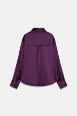 Camisa de cuello solapa y manga larga acabada en puño ancho, confeccionada en tejido satinado de color violeta. Cuenta con cierre frontal mediante botones dorados.