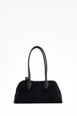 Cartera tipo bowling de diseño estructurado en color negro, con acabado aterciopelado y doble asa larga para llevar al hombro. Presenta un detalle de pequeña tira con broche metálico en la base de una de las asas.