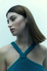 Top tejido color turquesa, sin mangas y con tirantes cruzados al frente que forman un nudo decorativo en el escote.
