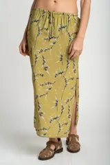Falda midi color verde oliva con estampado de ramas en negro y blanco. Tiene corte evasé, cintura alta con cordón ajustable y abertura lateral.