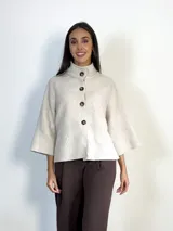Chaqueta tipo capa de lana bouclé en color marrón, con cuello mao y cierre frontal de botones grandes. Presenta mangas tres cuartos con puños ajustados de tejido acanalado.