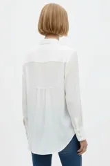 Camisa de seda negra de corte holgado, con cuello camisero y escote en V, cierre frontal con botones y dos bolsillos en el pecho.