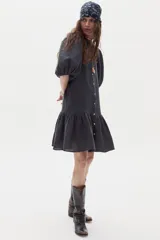 Vestido corto de lino color gris oscuro, con mangas abullonadas, cierre frontal con botones y volado en el ruedo.