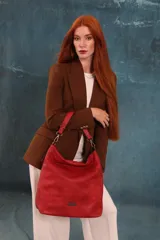 Cartera bandolera amplia de símil cuero color rojo, con asa corta fija y correa larga regulable. Presenta dos divisiones internas y un detalle metálico con el logo de la marca en el frente.