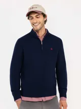 Sweater de punto acanalado en color azul marino, con cuello alto y cierre frontal parcial. Presenta mangas largas con puños acanalados y un pequeño logo bordado en rojo en el pecho.