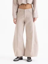 Pantalon de jean color beige, de corte wide leg con silueta redondeada y pinzas en las rodillas. Cuenta con cierre de botón y bragueta, bolsillos laterales y traseros, y detalles de remaches metálicos.