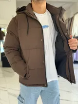 Campera puffer impermeable color beige con capucha desmontable con cordones negros, cierre frontal con cremallera y solapa con botones a presión.