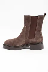 Bota tipo Chelsea de caña media, confeccionada en gamuza color marrón. Presenta paneles laterales elásticos al tono y una suela de goma robusta con plataforma baja y taco cuadrado.