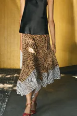 Falda midi de tiro alto con bajo asimétrico y cierre frontal cruzado con botón. Presenta un diseño que combina estampado de lunares y animal print.