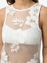 Vestido largo sin mangas confeccionado en encaje color crudo con diseño floral repetido en toda la superficie. Escote redondo y calce estándar. Prenda semi transparente.