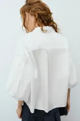 Camisa roja de cuello solapa, con mangas cortas abullonadas tipo globo y cierre frontal con botones ocultos.