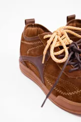 Championes urbanos de cuero vacuno en color marrón, con diseño de paneles superpuestos y costuras decorativas en zigzag. Presenta cordones bicolores y suela de goma al tono.