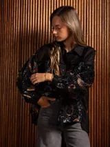 Camisa de manga larga con diseño de terciopelo estampado con motivos florales y paisley, combinada con paneles de tela transparente en la parte superior. Presenta cuello clásico, cierre frontal con botones y mangas abullonadas.