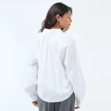 Camisa de popelina blanca con cuello clásico, cierre frontal de botones y mangas largas abullonadas con puños ajustados.