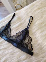 Conjunto de lencería compuesto por un bralette de encaje con breteles regulables y una tanga regulable con corte cola less. Ambas piezas presentan un diseño de encaje floral negro.