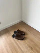 Zuecos marrones de cuero con tachas plateadas.