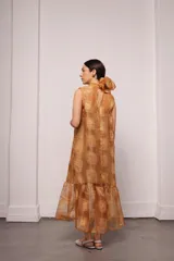 Vestido largo color ocre con estampado de cuadrados dorados, cuello alto y corte amplio. Incluye viso liso al tono.