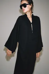 Vestido túnica largo negro de corte midi con mezcla de viscosa y lino, escote en V y mangas largas evasé. Presenta cierre frontal con alamares decorativos.