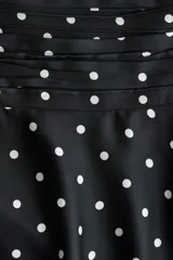 Pollera mini de satén negro con estampado de lunares blancos. Presenta una cintura ancha con pliegues horizontales y un diseño escalonado con volados que aportan volumen y movimiento.