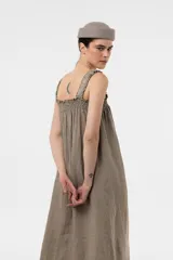 Vestido largo de lino color tostado, con silueta amplia, escote cuadrado con frunces elastizados y breteles anchos con detalles de volados.