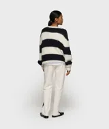 Suéter corto de punto grueso y peludo, con rayas horizontales anchas en blanco roto y negro. Presenta cuello redondo y mangas largas con puños anchos.