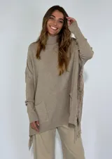 Sweater tostado de punto con cuello alto, corte holgado, bolsillo frontal y detalle de flecos en el lateral.