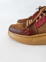 Zapatillas acordonadas de cuero marrón con detalles en rojo y suela de goma color caramelo.