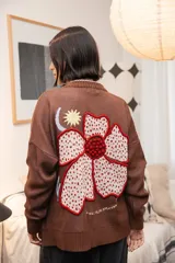 Saco tejido de punto color marrón con diseño de motivos orgánicos y florales. Presenta cierre frontal con botones, cuello redondo y mangas largas con puños acanalados. El diseño incluye detalles bordados que aportan textura y profundidad a la prenda.