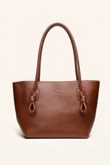 Cartera tote de cuero suave color marrón, con diseño amplio y líneas simples, con tiras de hombro decoradas con nudos artesanales y pequeño logo grabado en el centro.