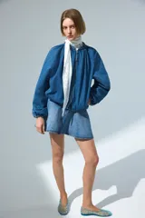 Campera bomber oversize de denim azul, con cuello elevado fruncido, cierre frontal y bolsillos laterales. Cuenta con mangas raglán y elásticos en puños y bajo.