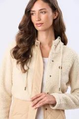 Campera de abrigo combinada en color beige, con parte superior de corderito y parte inferior capitoneada, capucha ajustable con cordones y cierre frontal con cremallera y broches.
