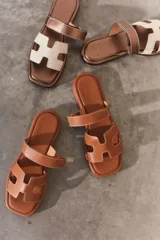 Sandalias planas de diseño minimalista en color tostado, con tiras anchas en forma de H y costuras a la vista. Poseen puntera cuadrada y suela plana.