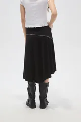 Falda midi negra de corte asimétrico, con detalle de costura diagonal decorada con pequeñas tachas metálicas.