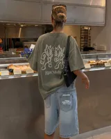 Remera marrón oversize de manga corta con estampado gráfico en la espalda de dos gatos de estilo retro con cuchillos y texto "Kahoa Industries".