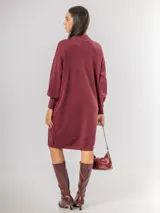 Vestido tipo polerón de tejido de punto color borgoña, con cuello alto, mangas largas con puños ajustados y corte recto. Incluye un cinturón del mismo material con una hebilla decorativa de flor con cristales.